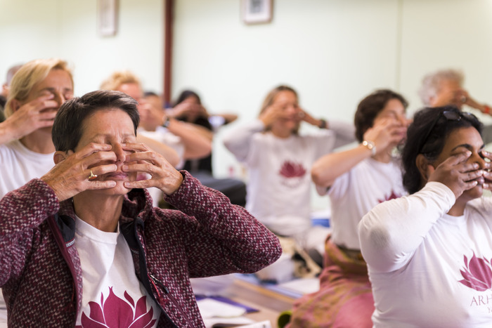 Cursisten oefenen ademhalingsoefeningen en volgen aanwijzingen tijdens een residentiële yogatraining